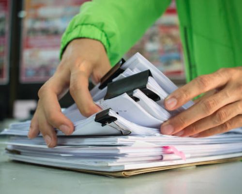 Businessman hands working in Stacks of paper files for searching information on work desk office, business report papers,piles of unfinished documents achieves with clip, Business concept